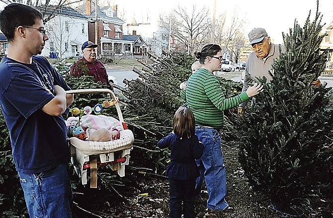 Tony Smith, Holts Summit, holds his 7-month-old daughter, Alissa, and waits as his wife, Jonni, center, holding two-year-old Lane, decides on a tree to buy Saturday afternoon. Optimist club members George Shull, second left, and Bob Phillips, holding the tree, were two of the volunteers helping out. 