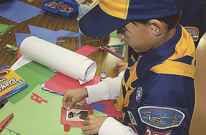 August Cross, 8, Mokane, carefully glues a photo of his grandfather onto an ornament for Cub Scout Pack 255's float for the Fulton Jaycees Christmas Parade. The Scouts' float this year will have a Christmas tree featuring ornaments with pictures of veterans. 