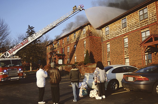 After gathering some belongings just in case, residents of 2227 Weathered Rock Road watch Jefferson City firefighters spray down the roof of their building to prevent the fire next door from spreading Monday afternoon. The fire was contained, but the 12-unit structure at left was heavily damaged. 