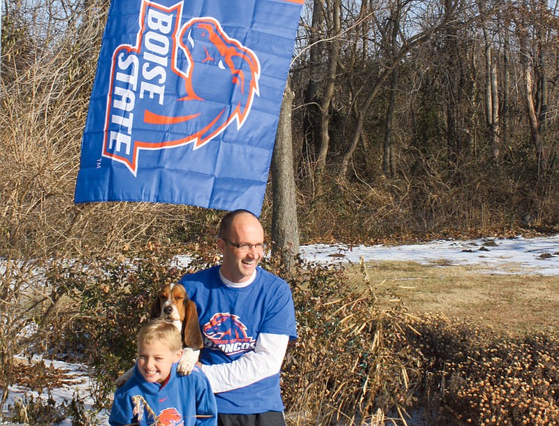 Don Norfleet/FULTON SUN photo: Ken Petterson with his son Aiden and Macgruber, his pet Bassett hound. Petterson Saturday morning mounted a new Boise State Broncos flag near his front door after the flag and an apology note appeared on his doorstep earlier in the day. Another smaller Boise State flag mounted on his house was stolen about two weeks ago.