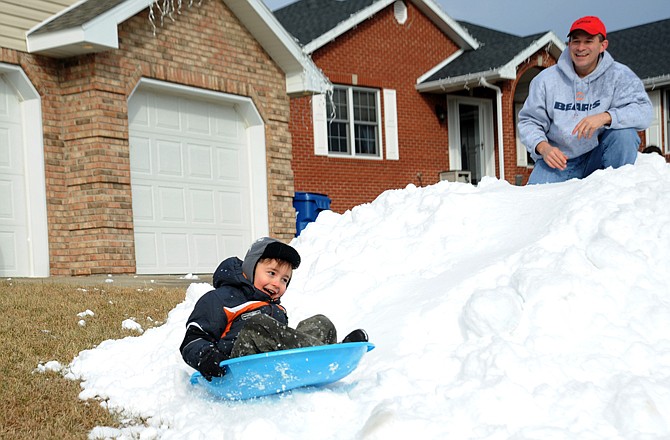 Adam Alonzo, 6, slides down a large pile of "snow" as his dad, Joe, watches Thursday in the family's front yard. Adam's mom, Cheryl Alonzo, won the Parks and Recreation Department's Guaranteed White Christmas Contest to promote the Washington Park Ice Arena, which provided the ice shavings.