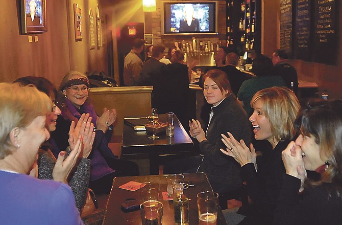 As Rebecca Neuenswander appears on the CBS Evening News, her mother Joyce Neuenswander and other HALO foundation members applaud during a watch party at Soggy Bottoms.