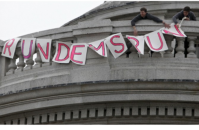 Two protesters put up a sign Thursday at the state Capitol in Madison, Wis., that reads "Run Dems Run" in support of 14 state senators that left the state in opposition to Gov. Scott Walker's bill to eliminate collective bargaining rights for many state workers. 