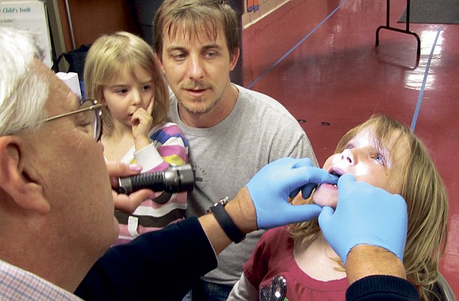 Dr. Bryan Pope of Small Smiles examines the teeth of Chloe Hughey, 7, as her dad, Jason Hughey, and little sister, Heidi, watch. The dental screening was part of Parents as Teachers Family Fun Night in Jefferson City.
