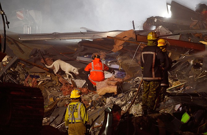 Emergency services workers and a dog search Tuesday through rubble for survivors of the collapsed CTV building in the business district of Christchurch, New Zealand. 