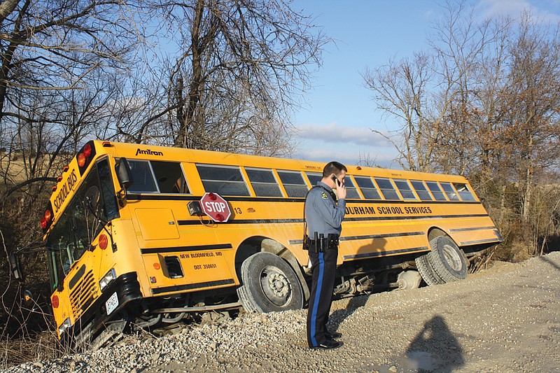 Mandi Steele/FULTON SUN photo: A New Bloomfield School District bus sits in a ditch off of Couny Road 432 Monday after it slid off the road. Trooper Andrew Armstrong of the Missouri State Highway Patrol investigates the accident.