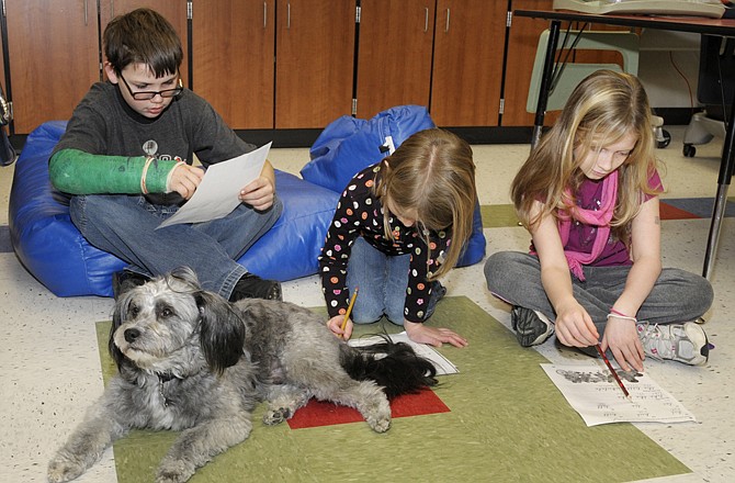 Chang, the South School therapy dog, rests comfortably at the feet of students Anthony Johnson, Josie Hall and Destiny Deluca as members of the Breakfast Club read or do homework before they go to their first class.