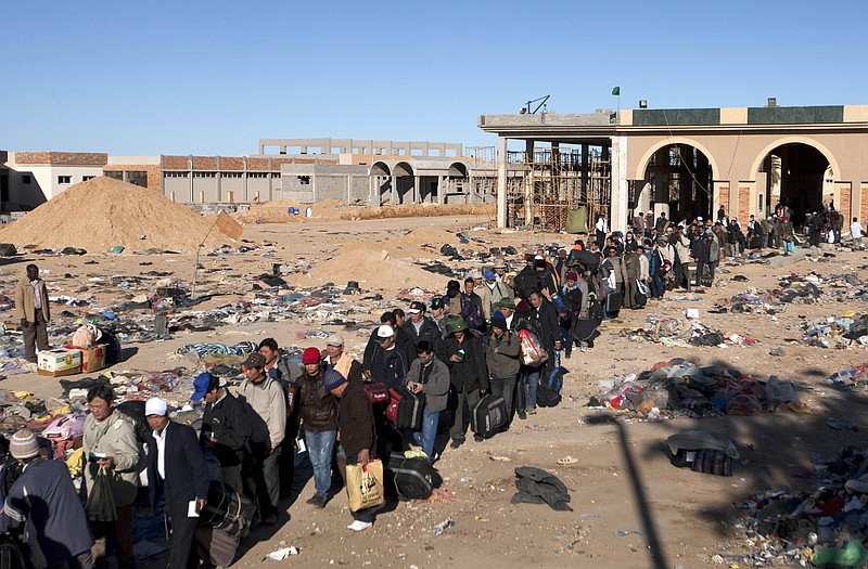 Refugees, many from the Philippines, wait in line Wednesday in Ras Ajdir, Tunisia, as they cross the border from Libya, in background, past debris and discarded items left by other refugees, at the Tunisia-Libyan border.