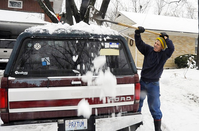 Charlie Skornia cleans the heavy snow off the top of his truck with a shovel Monday evening.