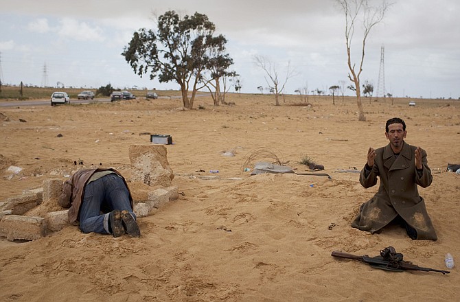 A Libyan rebel prays next to his gun Monday, while another one kneels over the grave of his dead brother, killed in the fighting, on the frontline of the outskirts of the city of Ajdabiya, Libya.