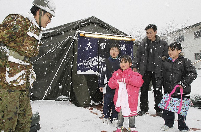 
Family members thank a Japanese soldier Wednesday after taking a bath set up inside a tent at the town of Yamada, northeastern Japan. Fears of radiation left many stores shelves bare of the staples and families wondering if it was safe for children to bathe.