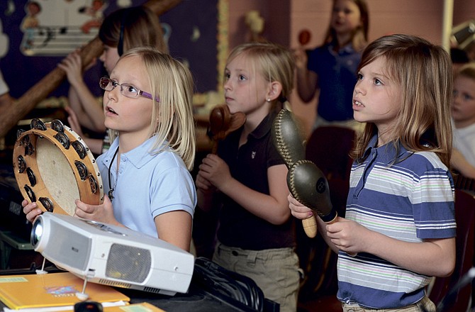 
St. Peter Interparish School students Aubrey Morff, left, Katie Farr, right, and Sophia Schepers watch the projection screen and follow along as they play a variety of instruments. 
