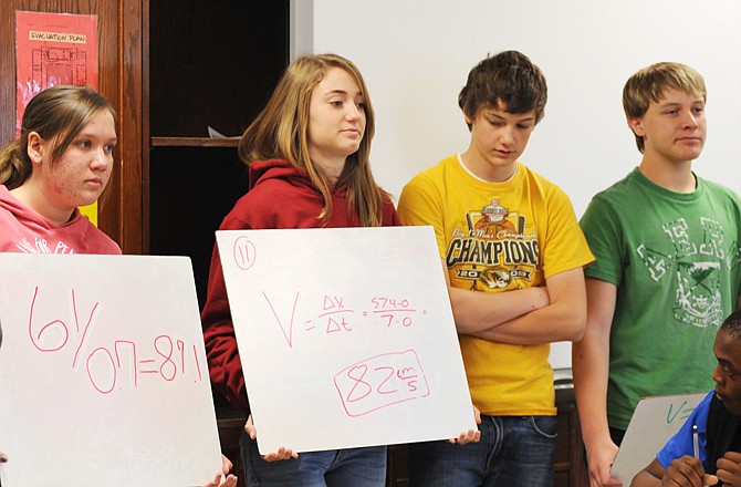 Simonsen Ninth Grade Center science students show their equations and how they drew those conclusions during Mike Hall's physics class. Katlyn Ottolini and Sarah Dumas hold the answers as teams tried to figure velocity given start and end points. Will Miller and Colton Henley, far right, wait their turns to explain their answers. Teachers have taken a hands-on approach to teaching the subject in an effort to make a better learning experience for the freshman students.
