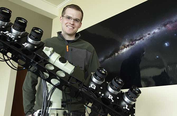 In this Monday, May 9, 2011 photo, Nick Risinger poses for a photo in Seattle with the rack of six synchronized astrophotography cameras he used to create the photograph on the wall behind him, which shows the entire night sky in a single composite image, made up of more than 37,000 exposures taken in different locations all over the world. 