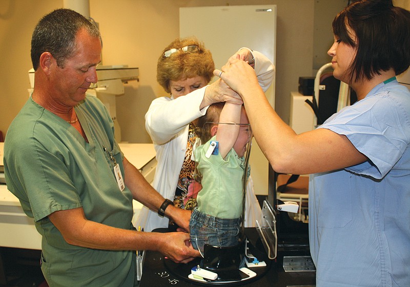 Sixteen-month-old Kaden Kleindienst, son of (far right) Ashley Gannaway, radiology student, demonstrates how the new child immobilization device works at Callaway Community Hospital. Steve Simerl, radiology technician, and Pat Schroeger, director of medical imaging, help strap Kleindienst into the device that secures a child during a chest X-ray.