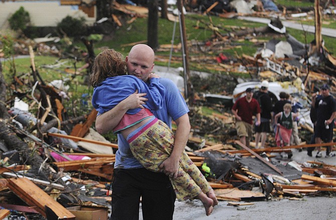 A man carries a young girl who was rescued after being trapped with her mother in their home after a tornado hit Joplin on Sunday evening. The tornado tore a path a mile wide and six miles long destroying homes and businesses.