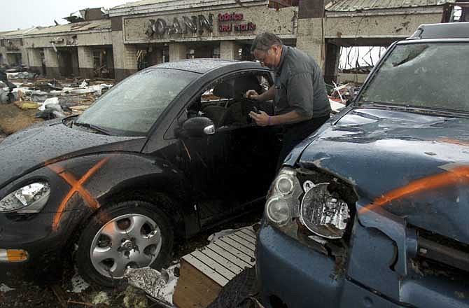 Scott Binns of Baxter Springs, Kan., searches for personal items in his family's tornado-damaged car at a shopping center in Joplin, Mo., Monday, May 23, 2011. A destructive tornado swept through Joplin on Sunday evening, killing at least 116 and injuring hundreds more. Binns' wife and daughter were in the fabric store seen at rear when the tornado struck and survived.