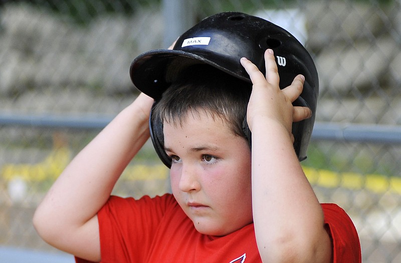 Max Hampton puts on his helmet in the Cardinals dugout before he takes his turn at bat Friday at Cosmo Field at Riverside Park.
