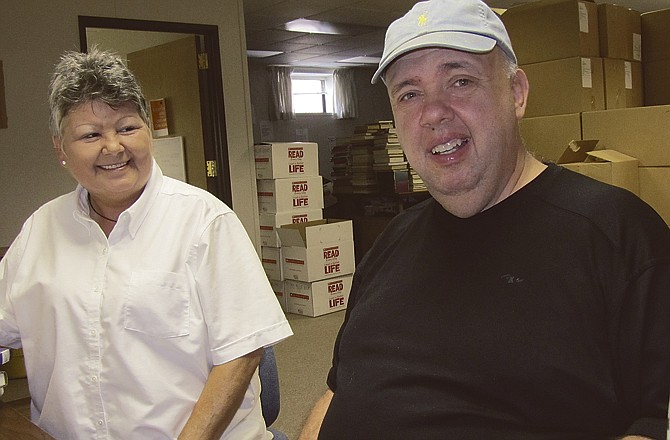 Greg Thurston stamps books removed from the collection Thursday morning at Missouri River Regional Library in Jefferson City. Thurston, 55, has volunteered for seven years. His personal attendant, Carol Rademann, is seated at left. 