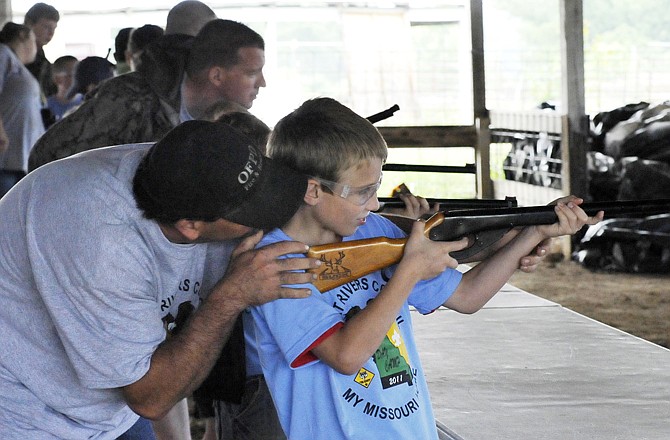 Roger Gerling helps his son, David, aim a BB gun at the firing range during Cub Scout Day Camp on Monday at the Jefferson City Jaycees Fairgrounds.