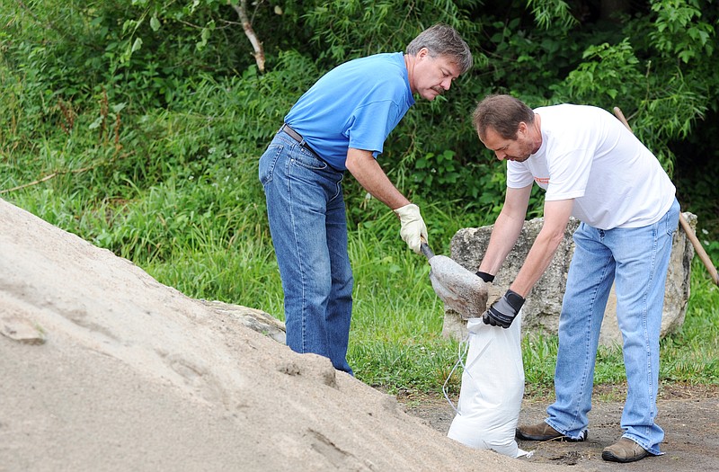 Rick Cox, left, and Everett Benson, fill sandbags Tuesday morning at the Salvation Army Thrift Store. After plastic was placed to cover a garage door opening, volunteers stacked the bags against the base of the building and garage door. Officials at the thrift store were worried that drainage from nearby Wears Creek would flood their basement.