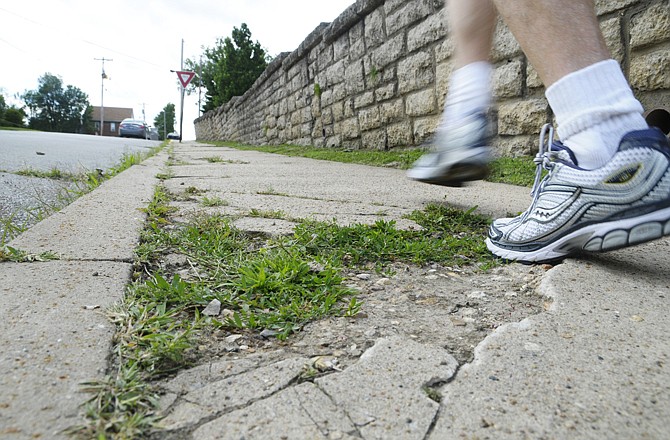 A runner steps in a hole in the broken concrete of the sidewalk on West Main Street.