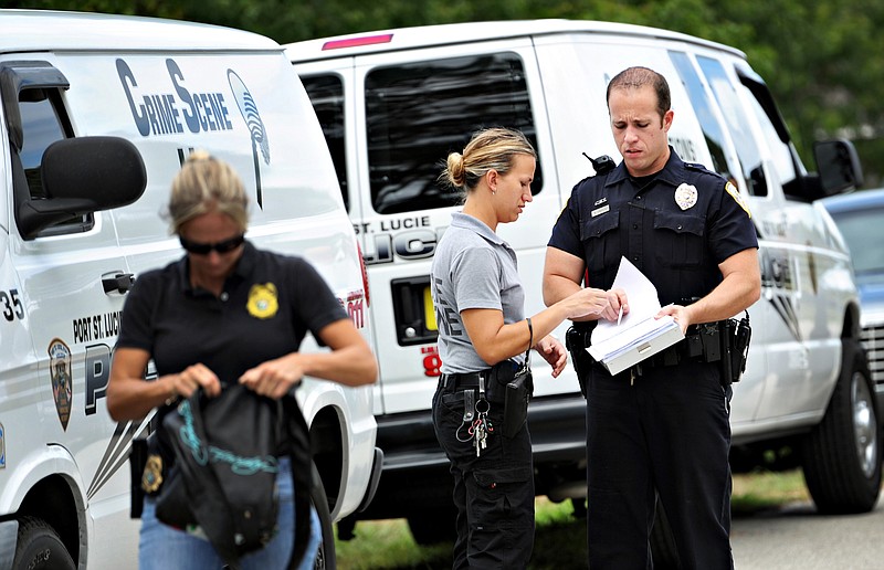 Port St. Lucie Police crime scene investigator Jeanine Hickox (center) talks Monday with a police officer at the crime scene in Port St. Lucie where a Florida teen is accused of posting a Facebook invite for a house party, killing his parents with a hammer and then hosting dozens of people while the adults' bludgeoned bodies were locked in the master bedroom. 