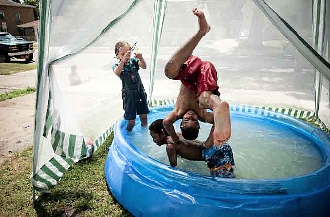 Nigel Crader, 12, of Flint, Mich., flips over Tyquavious Brown, 10, as Shamir Spencer, shields herself from the water while playing in a pool in their front yard on Mason Street in Flint on Tuesday, July 19, 2011. Hot and humid weather arrived this week and is forecast to remain into the weekend.