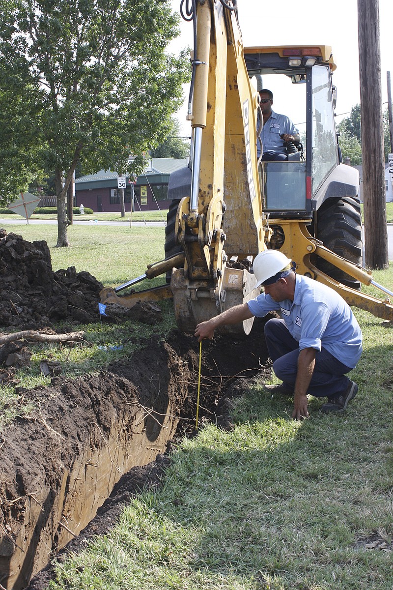 Jake Mosley, an employee of the Fulton Electric Department, Thursday measures the depth of a trench along St. Louis Avenue just west of Bluff Street where city overhead electric lines will be placed four feet underground. Operating the backhoe is Patrick Craighead of the Fulton Electric Department. Because of excessive heat, they are going to work at 6 a.m. and getting off at 2:30 p.m.