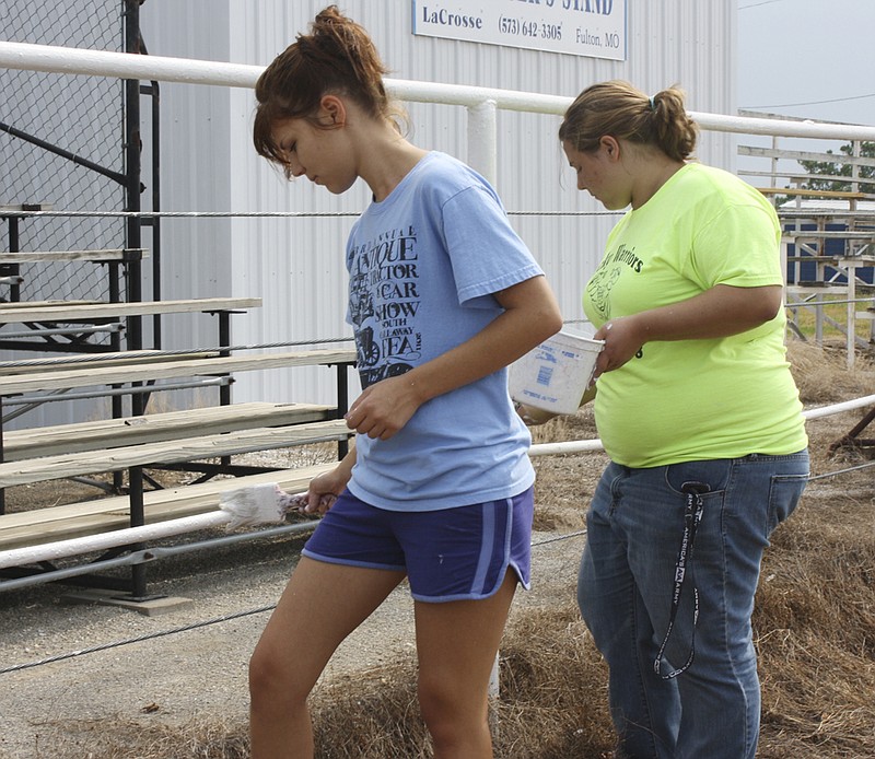 Ashley DuPont, left, and Natalie Bittle, were among about 30 volunteers who painted the Little Arena fence Saturday at the Kingdom of Callaway County Fairgrounds. Both are members of the South Callaway Future Farmers of America and both plan to to exhibit and sell hams they have smoked and salt cured at the fair, which opens Monday.