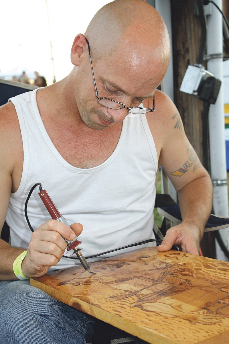 Fulton resident Greg Anderson darkens one of his wooden pictures at the Callaway County Fair on Thursday evening.