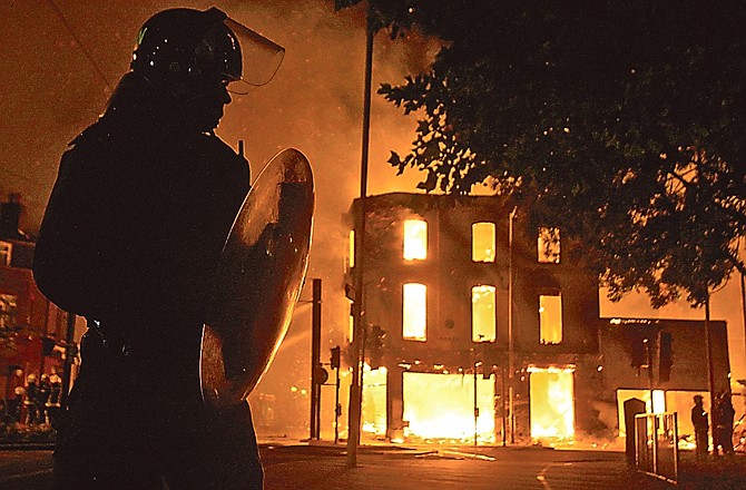 A building burns Monday as a riot police officer watches in Croydon, south London. Violence and looting spread across some of London's most impoverished neighborhoods on Monday.