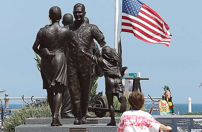 A boy rides his bicycle as a U.S. flag flies at half staff behind a Navy memorial statue of a homecoming in Virginia Beach, Va., where Navy Seal Team Six is based.