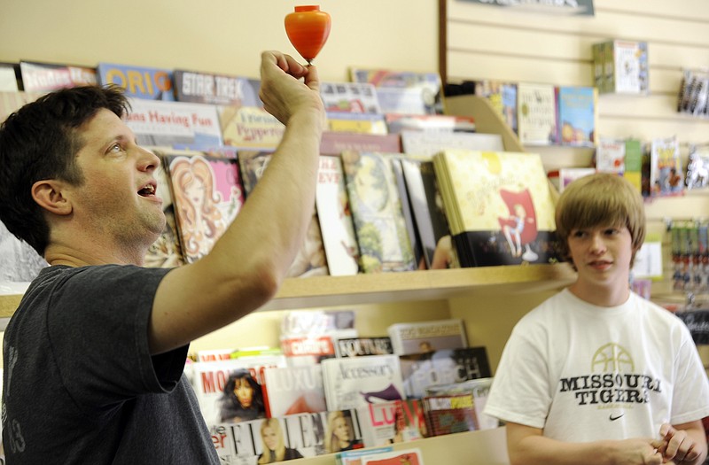 
Chris Neff, who is the new world spintop champion, demonstrates his technique Tuesday at Downtown Book and Toy for Josh Hickman, 14. Neff teaches weekly workshops on yo-yo and top spinning at the store.
