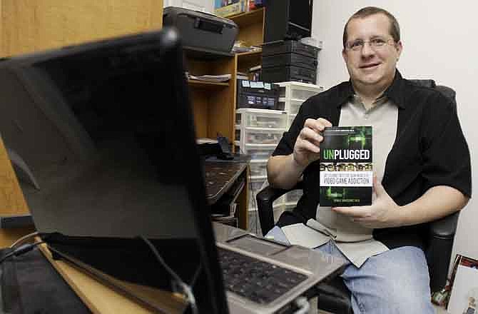 In this June 3, 2011 photo, Ryan Van Cleave holds a copy of his book "Unplugged" at his home in Sarasota, Fla. Gaming and thinking about video games was all-consuming for Van Cleave. Yet living inside the game World of Warcraft, which became his obsession, seemed preferable to the drudgery of everyday life. 