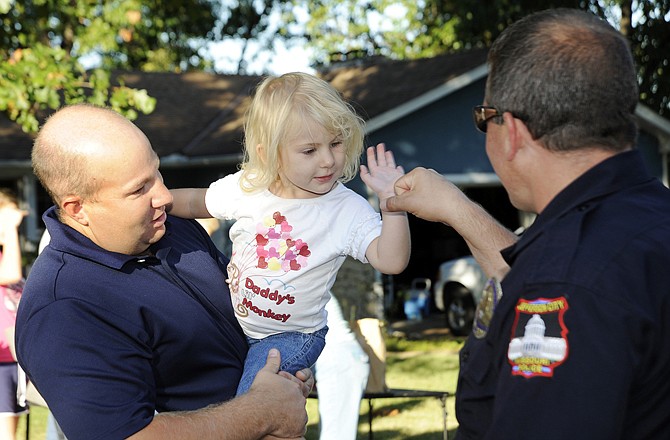 Jude Meldrem holds 2-year-old Lily as she high-fives Officer Les Martin before the National Night Out Against Crime meeting got underway Tuesday evening.