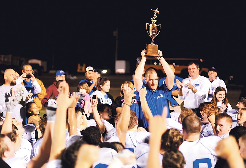 South Callaway head coach Tim Rulo (above) proudly displays the Callaway Cup trophy for the Bulldogs' players and fans after Friday night's 28-0 win over North Callaway at Kingdom City. South Callaway senior receiver-free safety Ben Seitz (right) tries to free himself from the grasp of North Callaway junior linebacker Ryan Pezold.