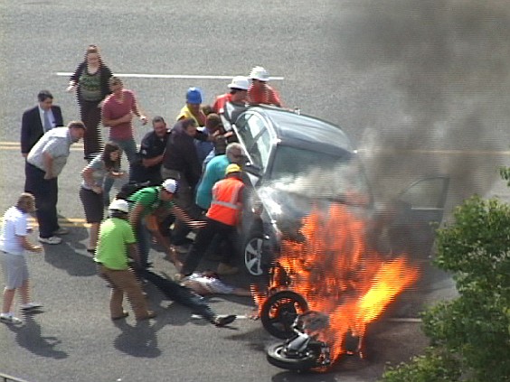 A group of people tilt a burning car Monday to free Brandon Wright, who was pinned underneath after an accident in Logan, Utah.  