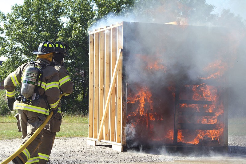 Fulton Fire Department firefighters rush in to put out the flames on a mock dorm Wednesday at the department. The room was torched in order to show William Woods University students how quickly a fire grows and how important early detection is.