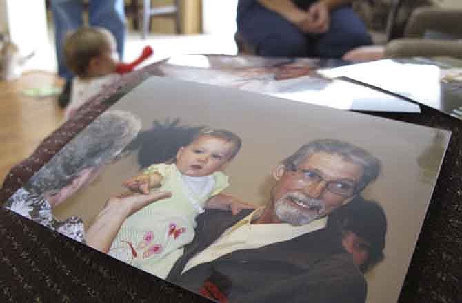 In this Sept. 1, 2011 photo, a print of Marshall McClain holding Alyssa, the girl he and his wife brought in to live with them in January 2011, sits on arm of a sofa in the McClains' Sharon, S.C. home as Alyssa plays on the floor in the background. For Marshall McClain, time had suddenly become the enemy. An infection raged through the 61-year-old Army veteran's withered, 115-pound frame, and the intravenous antibiotics couldn't keep up. 