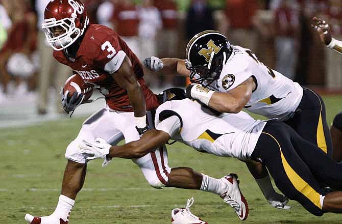 Oklahoma running back Brennan Clay, left, loses his shoe as he is tackled by two Missouri defenders in the second quarter of an NCAA college football game in Norman, Okla., Saturday, Sept. 24, 2011. 