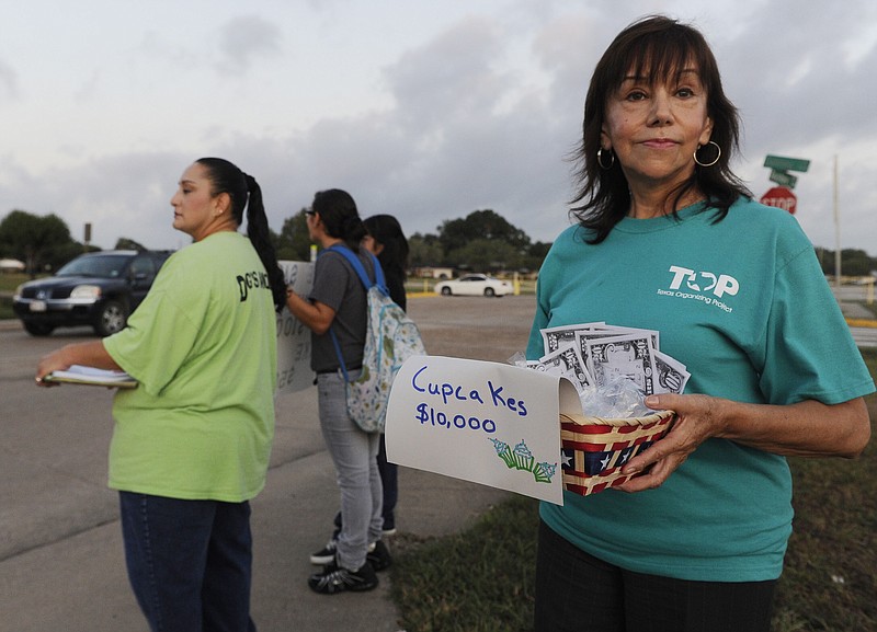 Angelica Garcia holds out a basket of phony money Monday at a school in Pasadena, Texas. Texas cities, counties and school districts may have to return more than $135 million, nearly half of it from public schools, to some of the nation's largest refineries should a commission grant them a tax refund. 