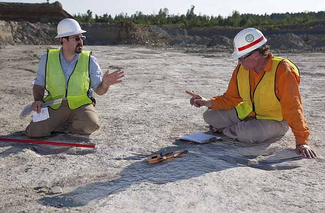 This July 12, 2011, photo provided by the University of Arkansas shows Geosciences professor Steve Boss, right, and colleagues Brian Platt discussing measurements of dinosaur tracks from a three-toed dinosaur being studied studied in Southwest Arkansas. The tracks, likely are from Acrocanthosaurus atokensis, one of the largest predators ever known, were found on private land in southwest Arkansas and provide a window into the life forms that roamed the area as long as 120 million years ago during the Early Cretaceous period.
