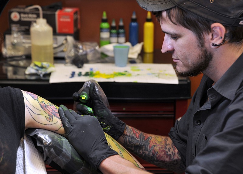 New business owner Shawn Pope applies ink with a dual coil machine to Katy Morris' arm Thursday at  Old Town Tattoos on East Dunklin. Pope said he prefers to design the artwork for his client's tattoos, such as the zombie girl for Morris.
