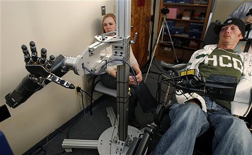 In this photo made Wednesday, Sept. 21, 2011, assistant professor Jennifer Collinger, left, watches as quadriplegic research subject Tim Hemmes operates the mechanical prosthetic arm in a testing sessions at a University of Pittsburgh Medical Center research facility in Pittsburgh. Hemmes had a chip implanted on the surface of his brain that reads his intention to move his paralyzed arm and sends that instruction instead to an advanced bionic arm. The goal is to create mind-controlled prosthetics to restore some independence to the paralyzed.