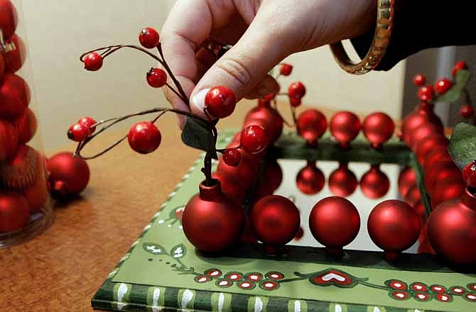 In this 2008 file photo, Jennifer Bertrand, of HGTV's "Christmas Crafts" online series, places decorative cranberries into the corner red balls on her holiday project, in Bloomington, Minn. Transforming your home into a festive wonderland for your family doesn't have to be expensive. Shoppers should first turn to their attic for any holiday scraps of holidays past --ribbons, pine cones and bows -- to see if they can be reused.