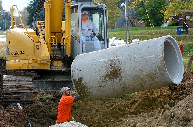 Matt Oligschlaeger lowers a section of concrete pipe while Nick Doerhoff, below, directs the piece into place. They are part of a crew from Stockman Construction Company that has been busy replacing the existing storm drain adjacent to East McCarty Street.