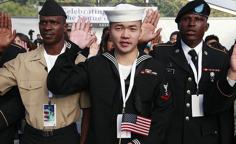 Zuyu Nu, center, from China and serving with the U.S. Navy, takes the oath of citizenship during a naturalization ceremony Friday at the Statue of Liberty. The oath of citizenship was taken by 125 people to mark the Statues's 125th anniversary. On the left is Adeniyi Ismail Rufai from Nigeria and serving with the Navy, and on the right is Patrick Kudzo Azameti from Ghana and serving the U.S. Army.