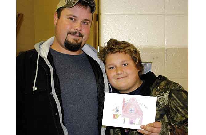 Fifth-grader Nicholas Staats, 11, holds up a Christmas card Friday he designed for the Callaway Community Hospital. The hospital recently held a contest to see whose design it would use for the cards. Josh Staats, left, came to South Callaway Elementary School in Mokane on Friday morning to congratulate his son on winning the contest. 