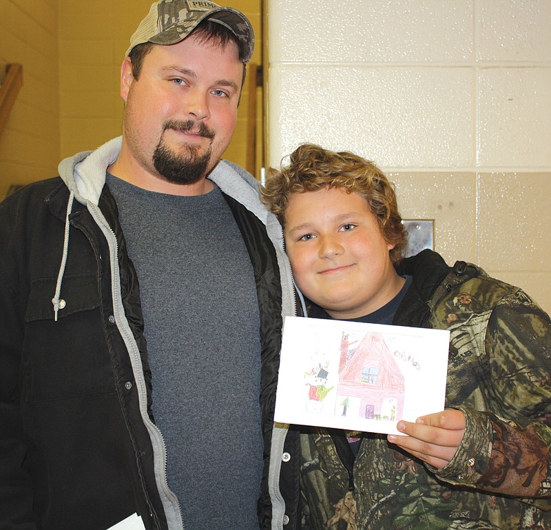 Fifth-grader Nicholas Staats, 11, holds up a Christmas card Friday he designed for the Callaway Community Hospital. The hospital recently held a contest to see whose design it would use for the cards. Josh Staats, left, came to South Callaway Elementary School Friday morning to congratulate his son on winning the contest.